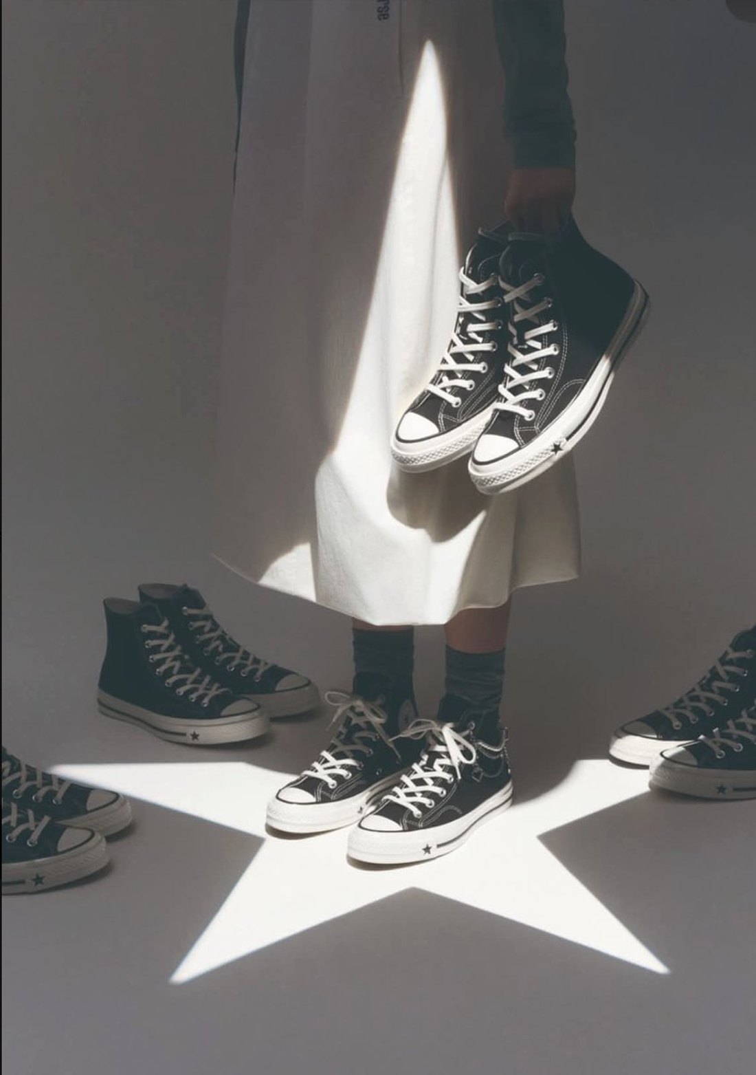 A studio photograph of canvas high top and low top sneakers arranged around a star shaped projection of light, with a figure holding one pair.